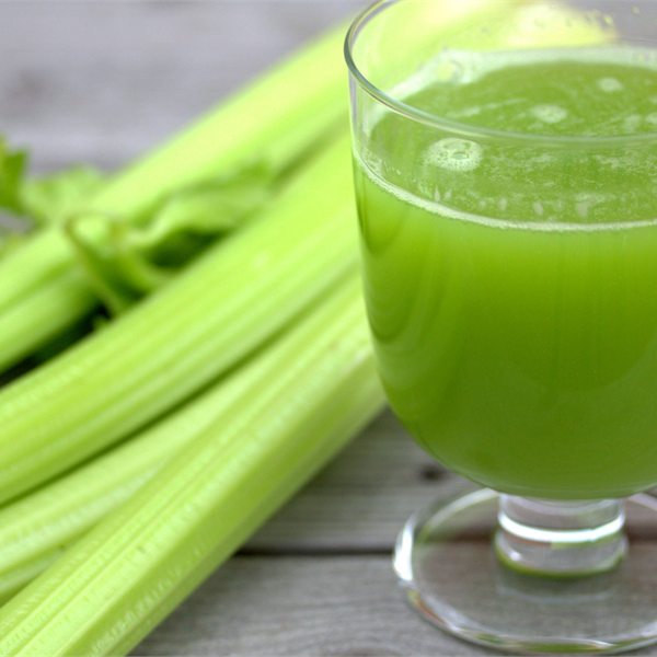 Grön sellerijuice i ett glas bredvid färsk selleri